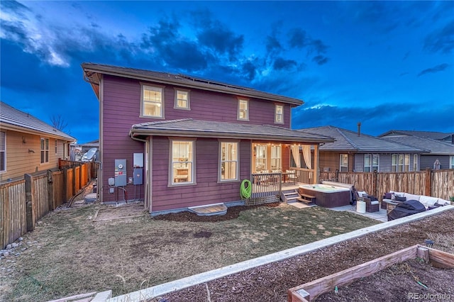 back of house at dusk with roof mounted solar panels, a fenced backyard, a hot tub, and an outdoor hangout area