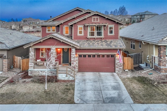 craftsman-style home with a garage, stone siding, fence, and concrete driveway