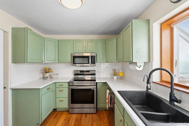 kitchen featuring backsplash, stainless steel appliances, sink, green cabinetry, and light hardwood / wood-style floors