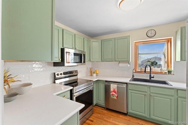 kitchen with backsplash, sink, green cabinetry, appliances with stainless steel finishes, and light hardwood / wood-style floors