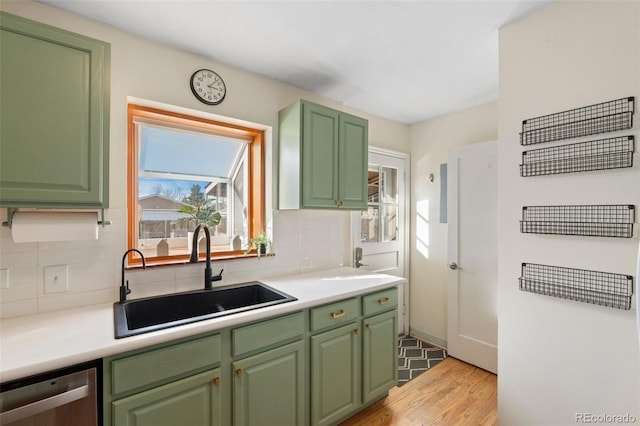 kitchen featuring backsplash, green cabinets, sink, light hardwood / wood-style flooring, and stainless steel dishwasher