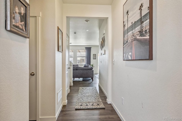 hall with dark wood-style flooring, visible vents, and baseboards