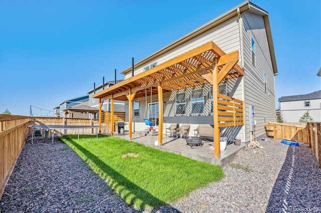 back of property with a trampoline, a lawn, a patio area, a fenced backyard, and a fire pit