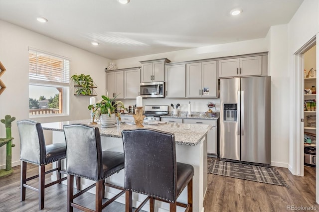 kitchen featuring appliances with stainless steel finishes, a breakfast bar, gray cabinetry, and light stone countertops