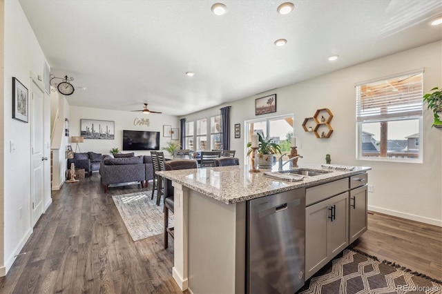 kitchen with a kitchen island with sink, gray cabinetry, open floor plan, stainless steel dishwasher, and light stone countertops