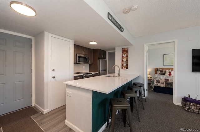 kitchen with appliances with stainless steel finishes, sink, a kitchen bar, a textured ceiling, and kitchen peninsula