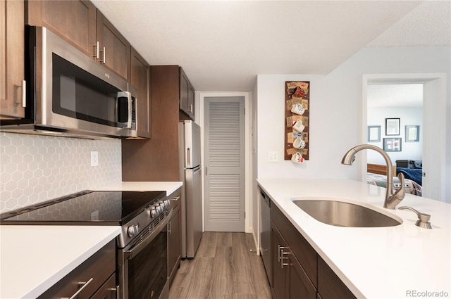 kitchen featuring light hardwood / wood-style flooring, dark brown cabinets, stainless steel appliances, sink, and tasteful backsplash