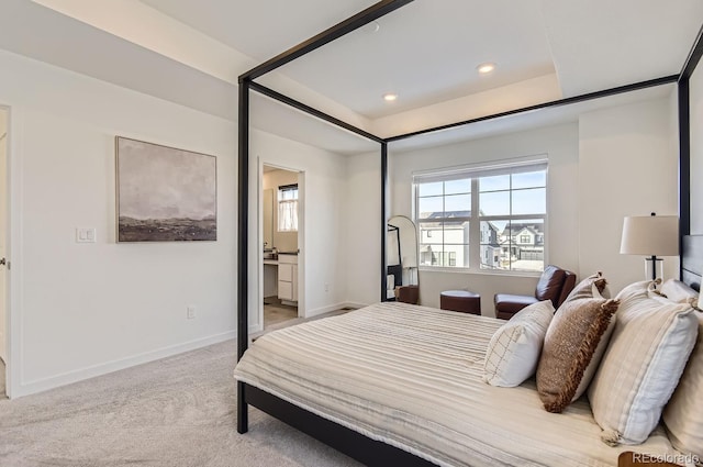 bedroom featuring a raised ceiling, ensuite bathroom, and light carpet