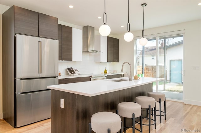 kitchen featuring pendant lighting, sink, appliances with stainless steel finishes, a kitchen island with sink, and wall chimney exhaust hood