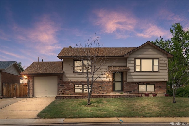 bi-level home with driveway, brick siding, an attached garage, and roof with shingles