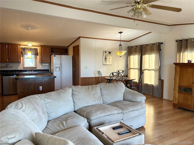 living room with vaulted ceiling, ceiling fan, crown molding, a textured ceiling, and light hardwood / wood-style flooring