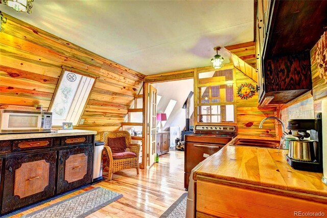 kitchen featuring light hardwood / wood-style floors, white range with electric cooktop, vaulted ceiling with skylight, and sink