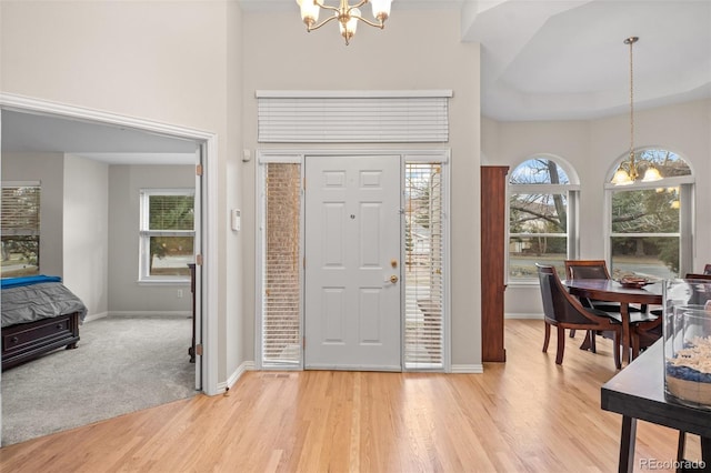 entryway featuring an inviting chandelier, a towering ceiling, baseboards, and light wood finished floors