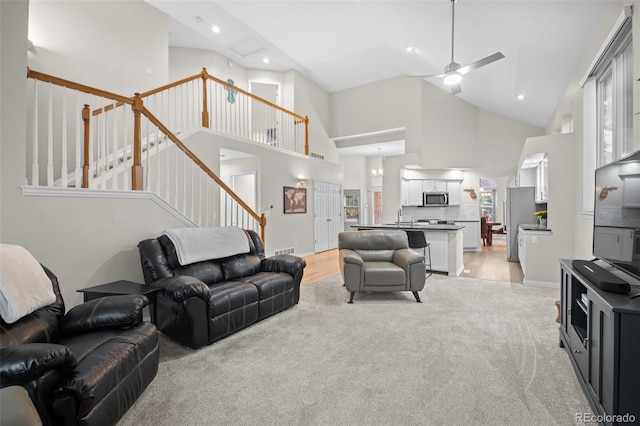 living room with stairway, light carpet, a ceiling fan, and high vaulted ceiling