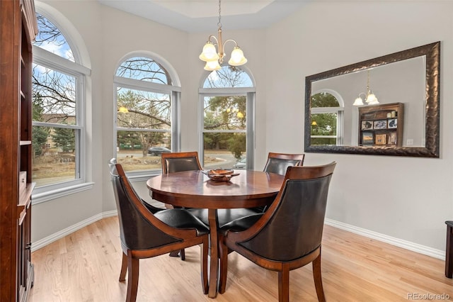 dining area with light wood finished floors, an inviting chandelier, baseboards, and a high ceiling
