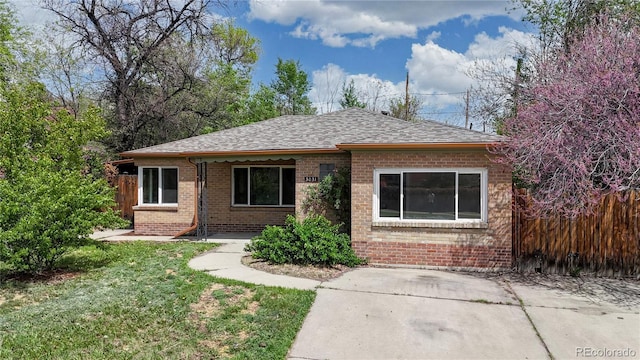 view of front of home with roof with shingles, fence, brick siding, and a front yard