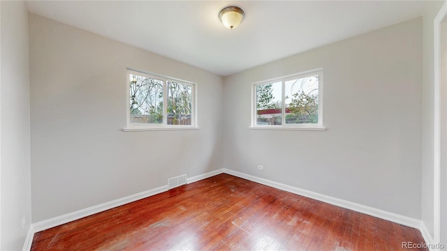 unfurnished room featuring baseboards, visible vents, and wood finished floors