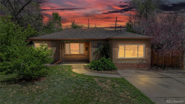 view of front of house featuring a shingled roof, a front lawn, and brick siding