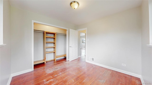 unfurnished bedroom with wood finished floors, baseboards, and a closet