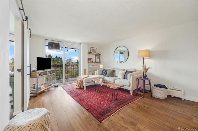 living area with floor to ceiling windows, a textured ceiling, a barn door, wood-type flooring, and a baseboard heating unit