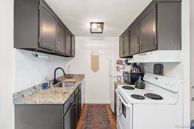 kitchen featuring dark wood finished floors, a sink, baseboards, under cabinet range hood, and white appliances