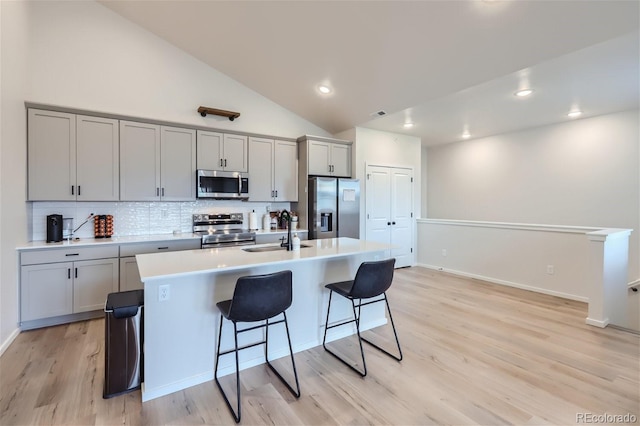 kitchen with stainless steel appliances, a center island with sink, gray cabinets, and sink