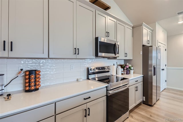 kitchen featuring light hardwood / wood-style flooring, tasteful backsplash, lofted ceiling, white cabinets, and appliances with stainless steel finishes