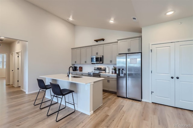 kitchen with a breakfast bar, a sink, appliances with stainless steel finishes, gray cabinets, and light wood-style floors