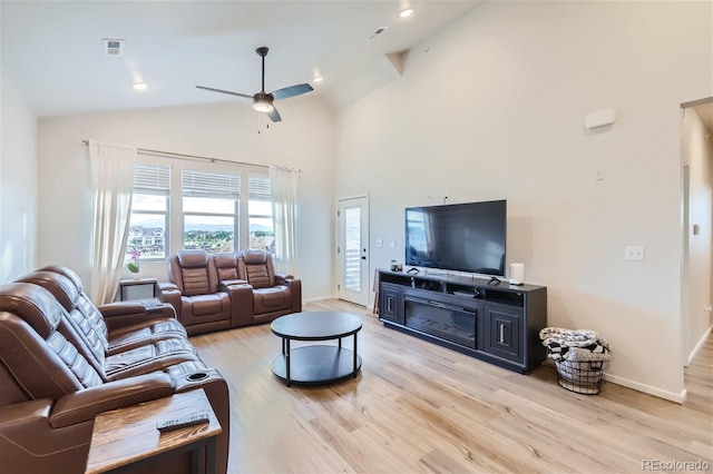 living area with high vaulted ceiling, ceiling fan, baseboards, and light wood-type flooring