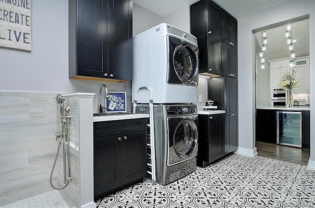 laundry room with cabinets, light tile patterned flooring, stacked washer and dryer, wine cooler, and sink