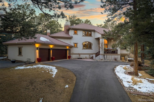 mediterranean / spanish home with a tile roof, stucco siding, a chimney, a garage, and driveway