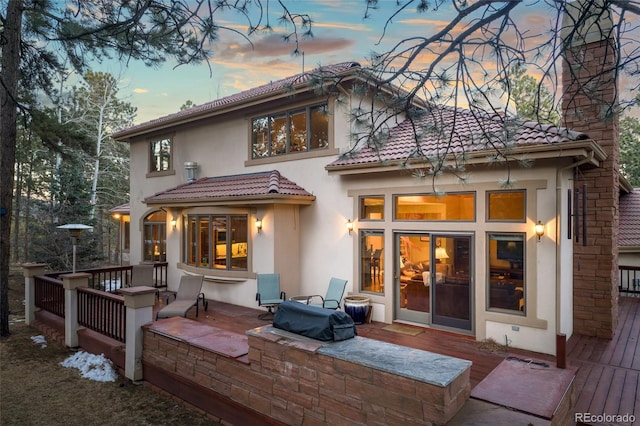 back of property at dusk with stucco siding, a tiled roof, and a wooden deck