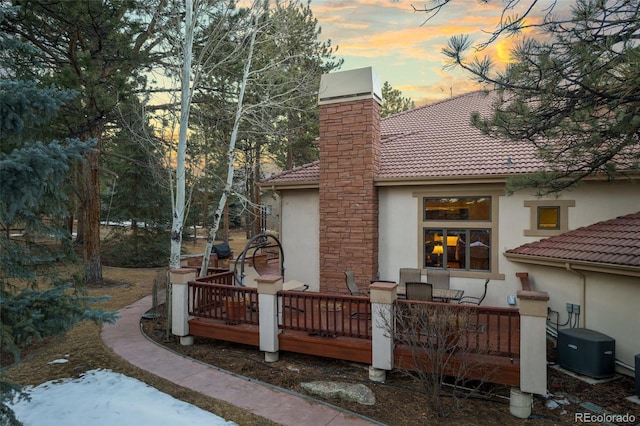 rear view of house with a tile roof, a chimney, a wooden deck, and stucco siding