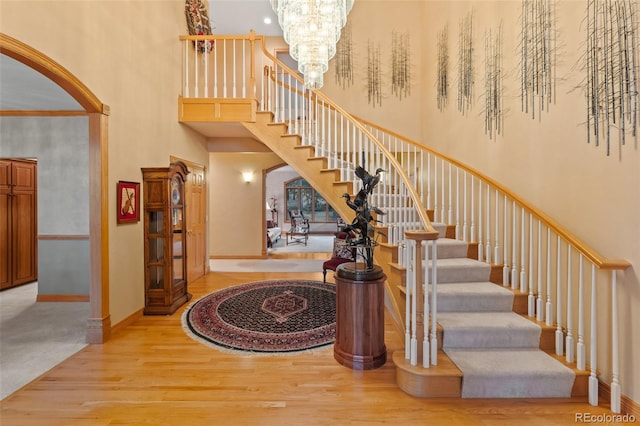 stairway featuring arched walkways, a notable chandelier, a high ceiling, wood finished floors, and baseboards