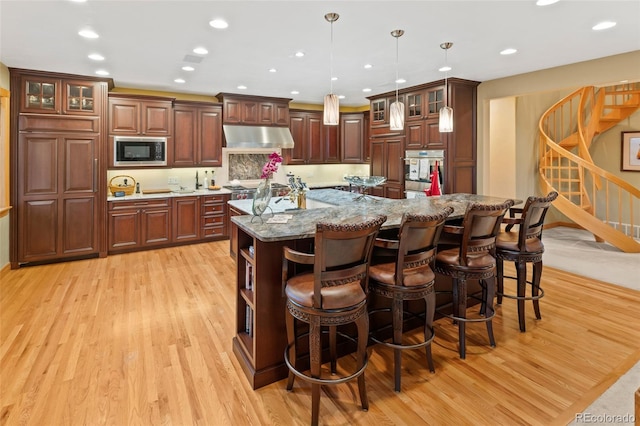 kitchen with under cabinet range hood, a breakfast bar area, stainless steel appliances, and light wood-style floors