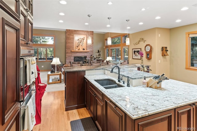 kitchen with a fireplace, wall oven, light wood-style floors, a sink, and a large island with sink