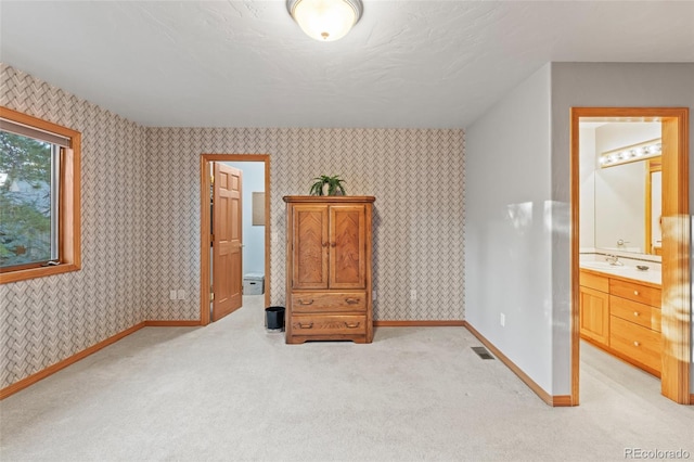 bedroom featuring wallpapered walls, baseboards, a sink, and light colored carpet