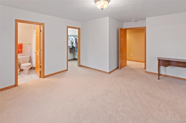 unfurnished bedroom featuring baseboards, a spacious closet, and light colored carpet