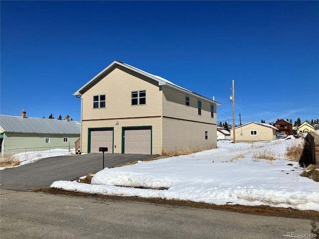 view of snowy exterior with driveway and an attached garage