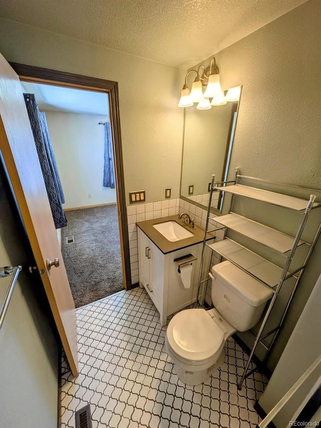 bathroom with visible vents, toilet, vanity, a textured wall, and a textured ceiling