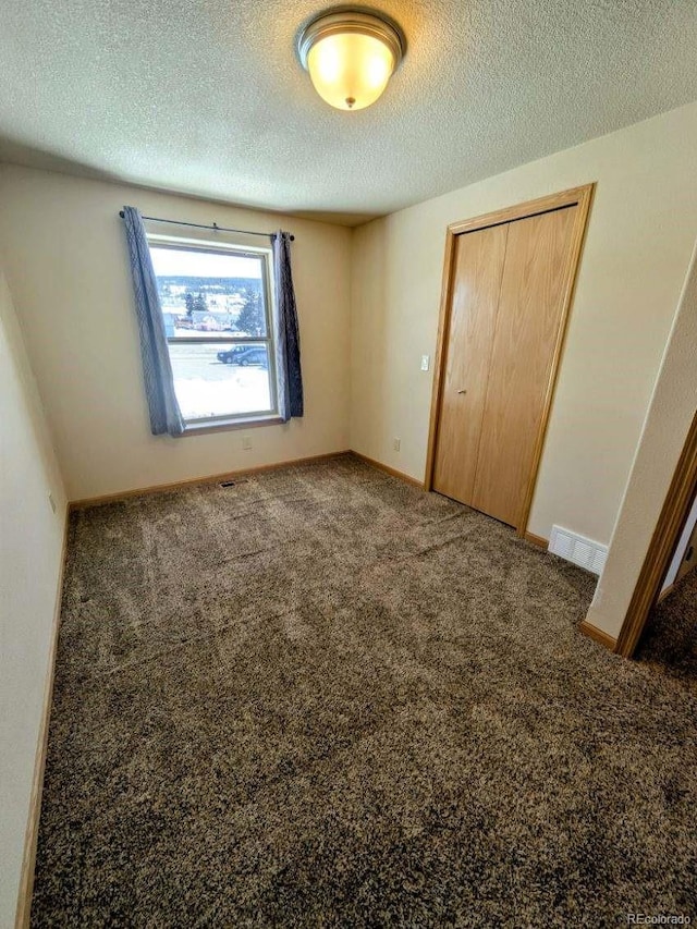 unfurnished bedroom with visible vents, a textured ceiling, a closet, carpet flooring, and baseboards