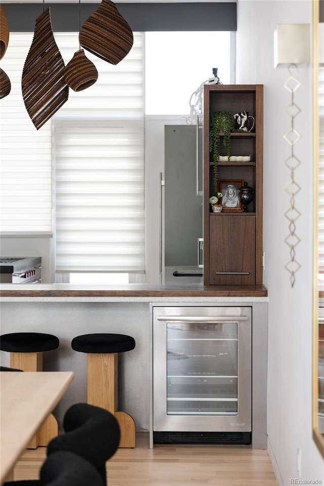 bar featuring stainless steel fridge, light hardwood / wood-style floors, and beverage cooler