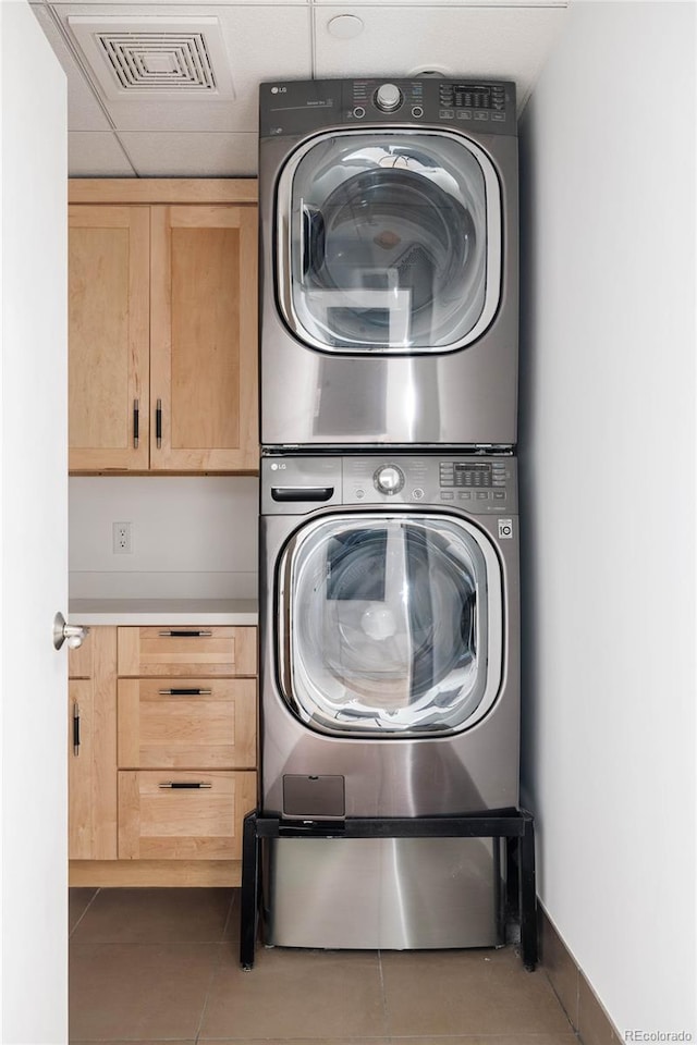 clothes washing area with cabinets, stacked washer and clothes dryer, and tile patterned floors