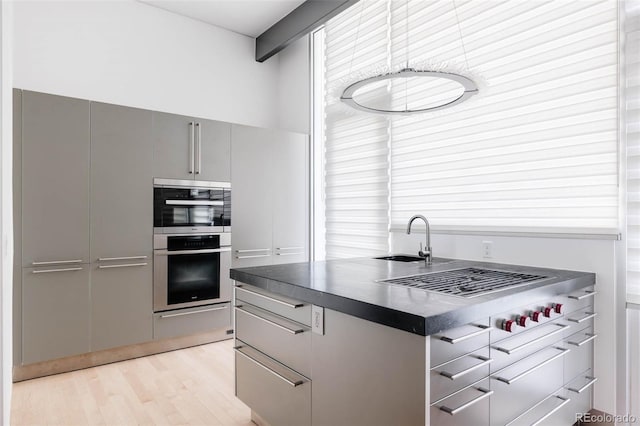 kitchen featuring dark countertops, gray cabinetry, double oven, light wood-style flooring, and a sink