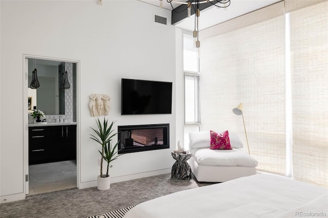 bedroom featuring visible vents, a glass covered fireplace, connected bathroom, carpet, and a towering ceiling