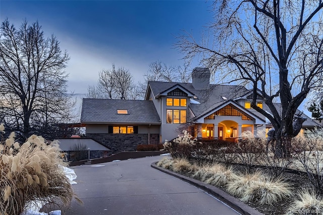 view of front of property featuring stone siding, a chimney, driveway, and stucco siding