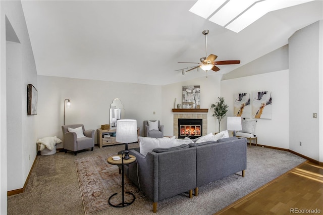 living room with wood finished floors, lofted ceiling with skylight, a tile fireplace, and a ceiling fan