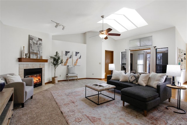 living room featuring a fireplace, a skylight, a ceiling fan, baseboards, and track lighting