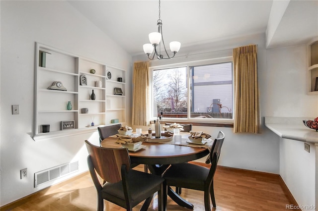 dining area featuring lofted ceiling, a notable chandelier, visible vents, and wood finished floors