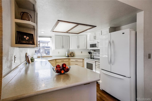 kitchen featuring dark wood-style floors, light countertops, a sink, white appliances, and a peninsula